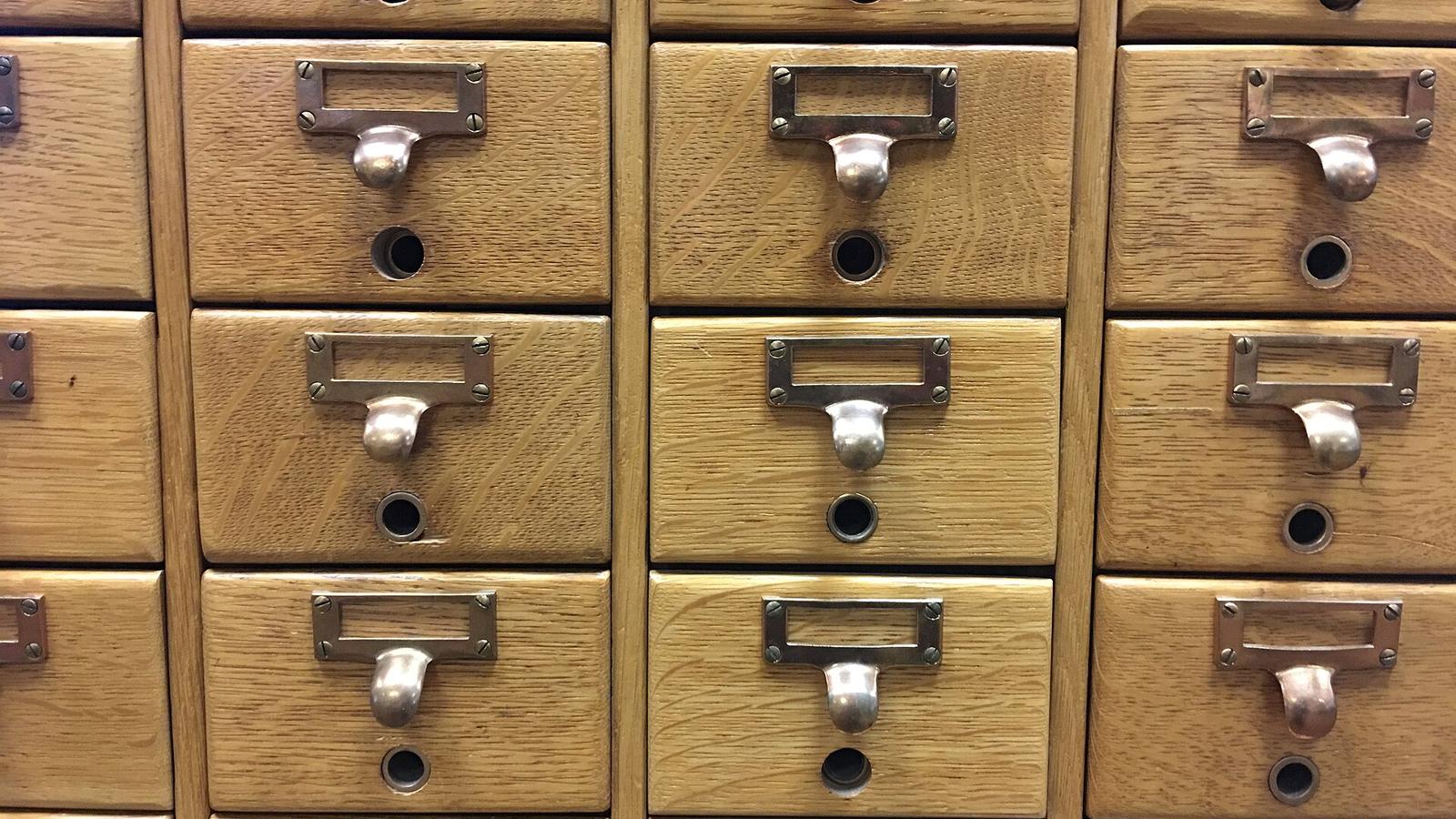 Rows of small wooden drawers with metal label holders in an old library card catalog